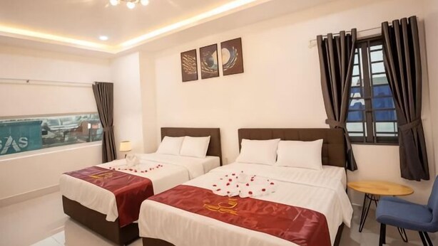 Habitación de hotel con dos camas, una mesita, una silla y vistas a la ciudad.