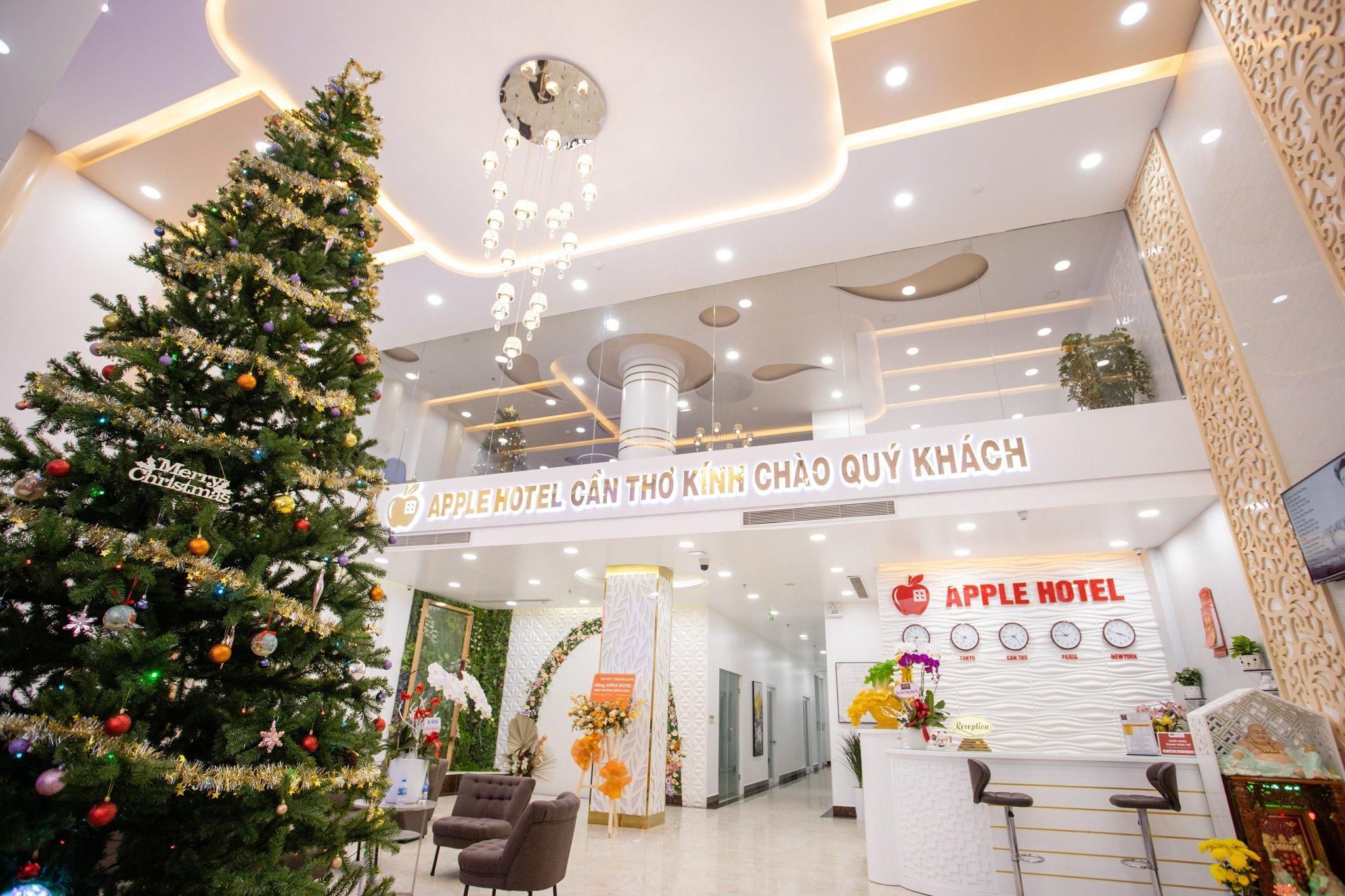 A hotel reception area with a Christmas tree, a reception desk, and a sign for the Apple Hotel.
