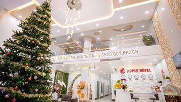 A hotel reception area with a Christmas tree, a reception desk, and a sign for the Apple Hotel.