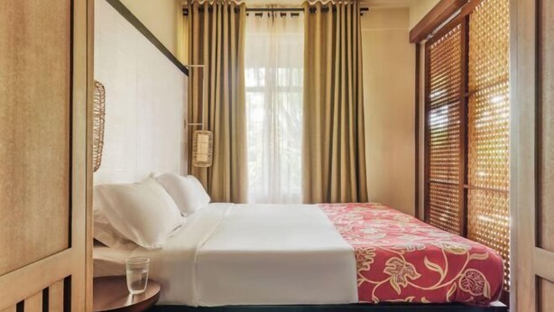 Una habitación de hotel con una cama, una mesita de noche con un vaso de agua y cortinas.