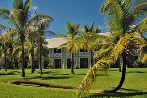 Un bâtiment à la façade symétrique, entouré d’une pelouse bien entretenue et de palmiers.