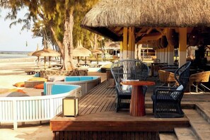 Un salon de plage doté de parasols en chaume, de meubles en osier et d’une terrasse en bois offrant une vue sur la mer.