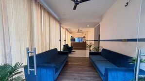 A modern hotel lobby with two blue sofas, a reception desk, and a staircase in the background. - Celebration Park (Gobindpur)
