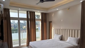 A modern bedroom with a large bed, a ceiling fan, and a view of a balcony. - Celebration Park (Gobindpur)