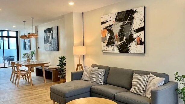 A modern living room with a grey sectional sofa, a round coffee table, and a dining area with wooden furniture. - Private & Cozy house, Chiang Rai Airport (Chiang Rai)