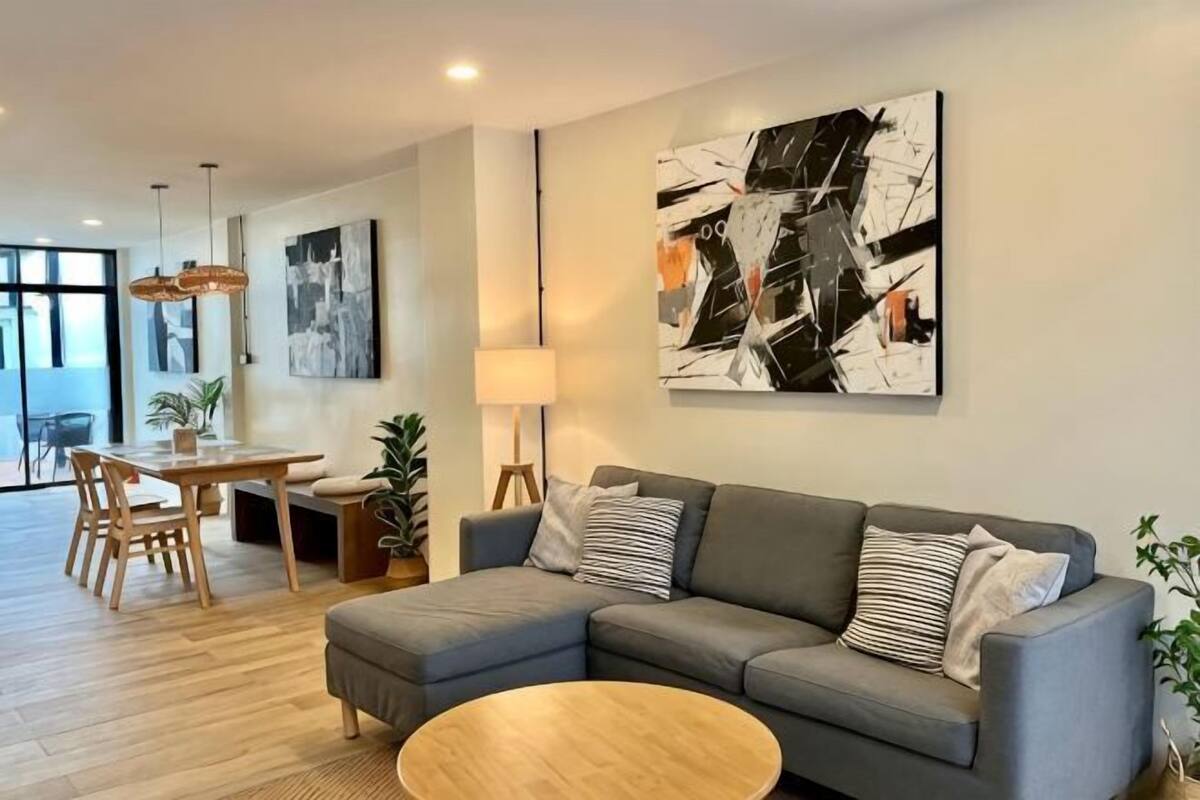 A modern living room with a grey sectional sofa, a round coffee table, and a dining area with wooden furniture.