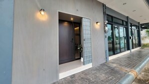 A modern building with a dark entrance door, glass doors, and a tiled walkway. - Private & Cozy house, Chiang Rai Airport (Chiang Rai)