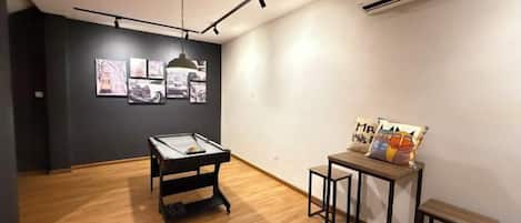 Una habitación con una mesa de billar, una pequeña mesa con libros y un aire acondicionado de pared.