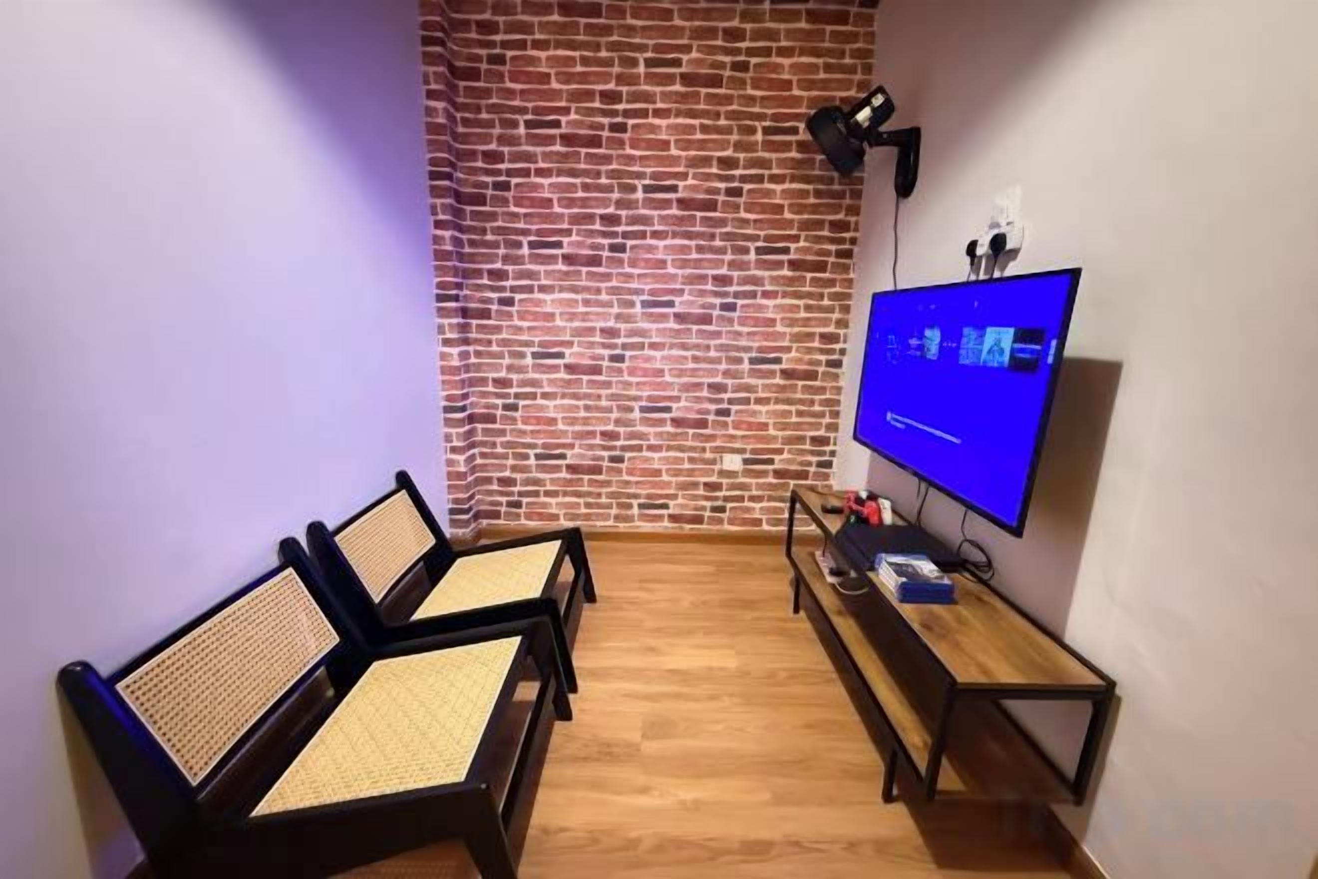 Une pièce avec un mur en briques, deux chaises en bois, un téléviseur et une petite table.