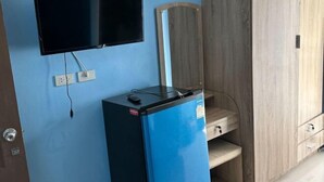 A room with a flat-screen TV mounted on the wall, a blue refrigerator, and a wooden wardrobe with multiple drawers. - Mildmint Self Serviced (Phuket)