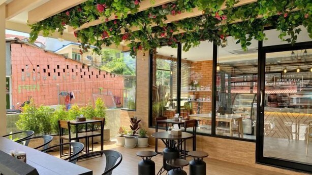 An indoor café with tables and chairs, a brick wall, and a large window. - Mildmint Self Serviced (Phuket)