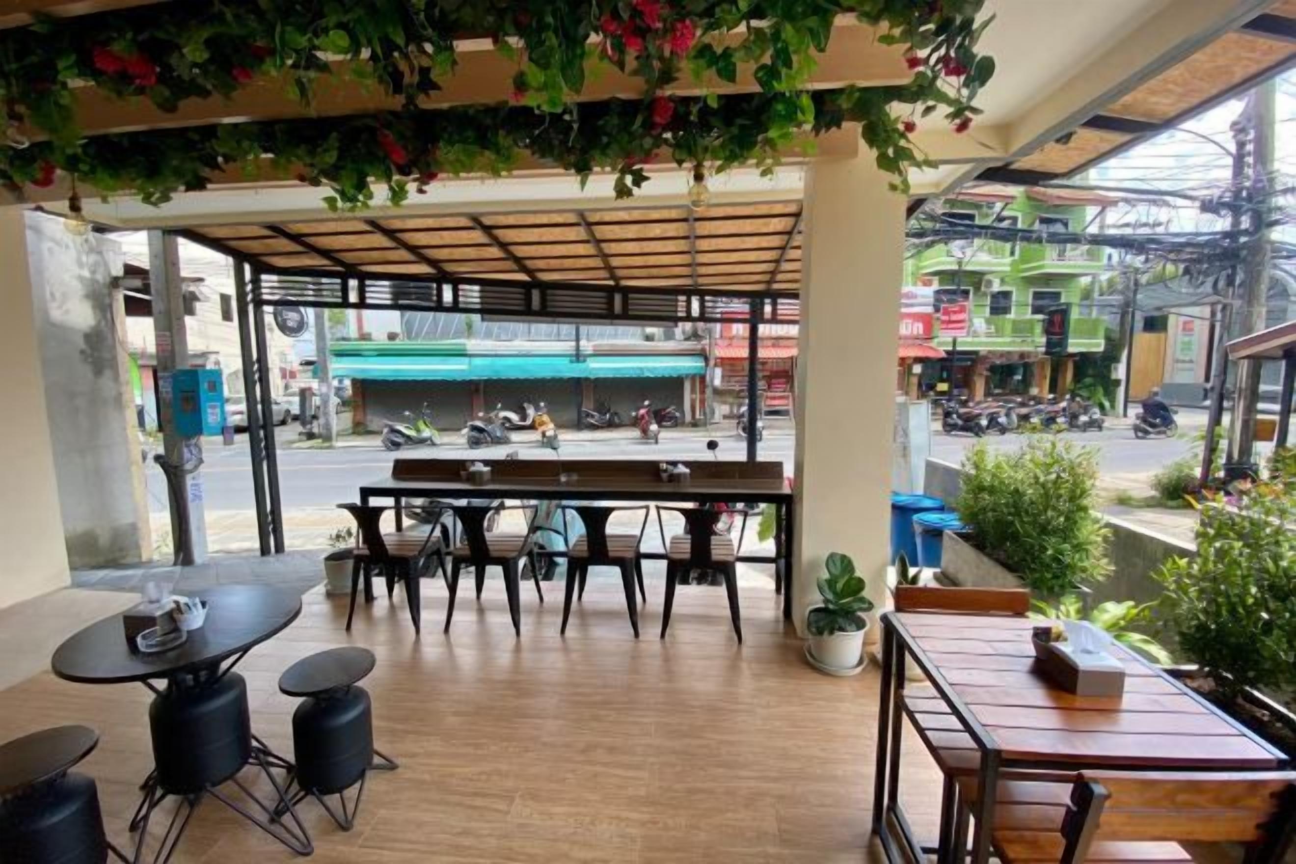 An outdoor seating area with tables and chairs, a view of the street, and potted plants.
