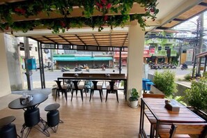 Zona d'estar a l'exterior amb taules i cadires, vista al carrer i plantes en testos.