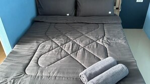 A bed with a quilted grey duvet, two pillows, and a rolled grey towel. - Mildmint Self Serviced (Phuket)