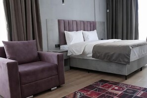 Ein modernes Schlafzimmer mit einem Bett, einem Nachttisch, einem Sessel und einem gemusterten Teppich.