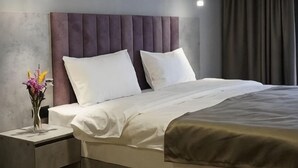 A neatly made bed with white linens, a headboard, and a bedside table with a vase of flowers.
