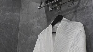 A white textured robe hanging on a black hanger against a marble wall.