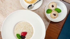 A dessert plate with a berry and mint garnish, a cup of coffee with a spoon, and a plate with two cookies and mint leaves.