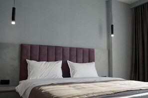 A modern hotel room with a large bed, a headboard, and pendant lighting.