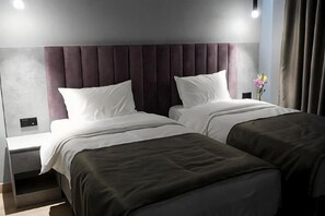 A hotel room with two beds, a nightstand, a wall-mounted light, and a window with curtains. - ASYR Expo Hotel (Astana)