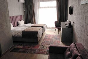 Ein Hotelzimmer mit zwei Betten, einem Schreibtisch, einem Stuhl, einem gemusterten Teppich und Blick ins Freie.