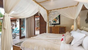 A bedroom with a canopy bed, wooden furniture, a view of the outdoor area, and a painting on the wall.