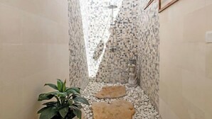 A narrow, tiled shower area with a mosaic pattern, a statue, and a potted plant.