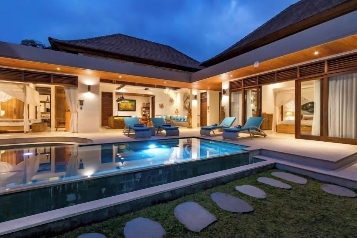 A modern outdoor pool area with lounge chairs, a well-lit interior, and a clear sky.