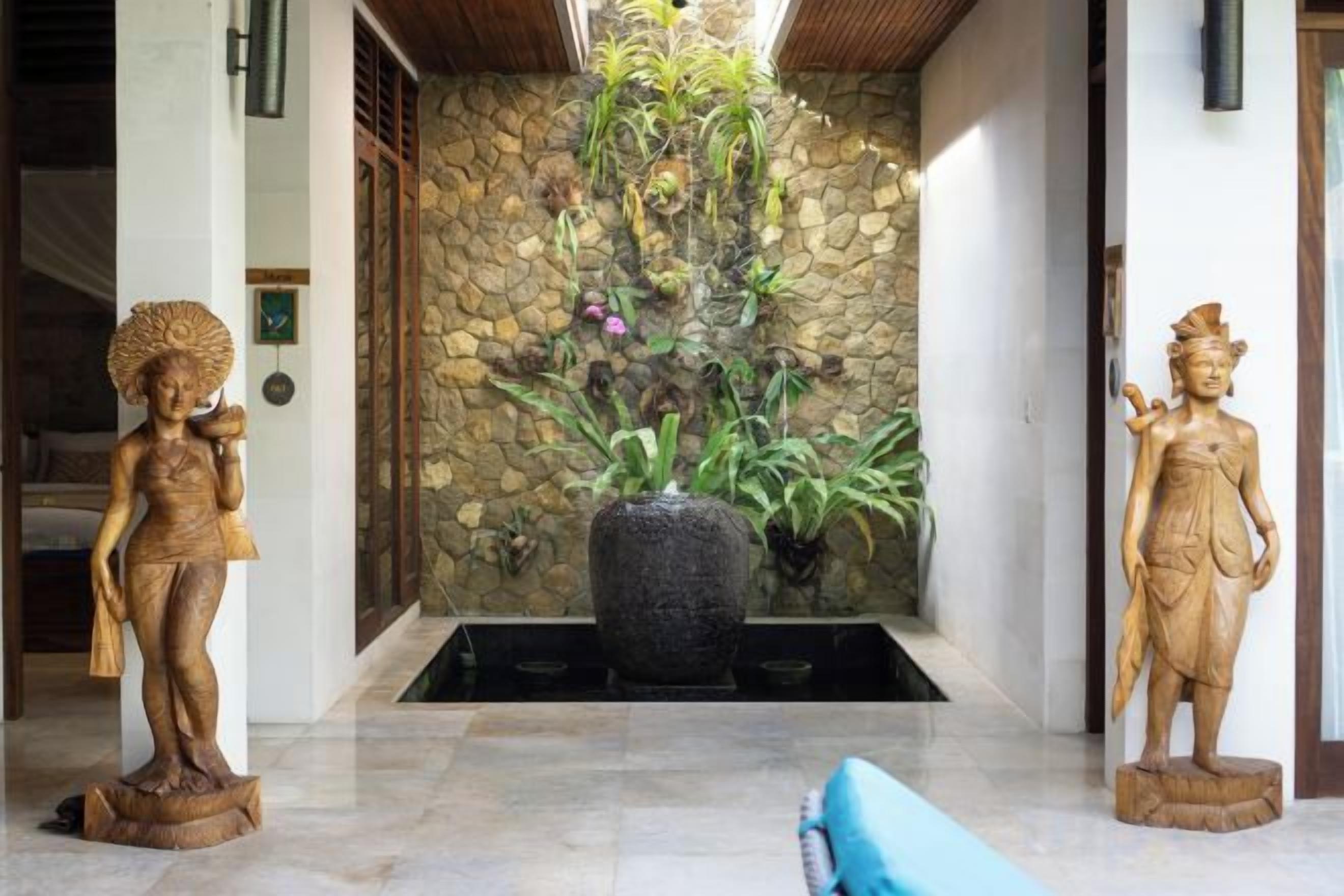 A stone wall with a water feature and two wooden statues in a lobby area.