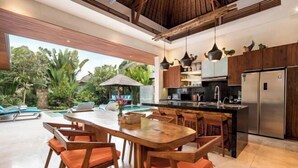 A modern kitchen with a central island, wooden dining table, and chairs, with a view of a pool and lush greenery outside. - Villa Liang Ubud (Bali)