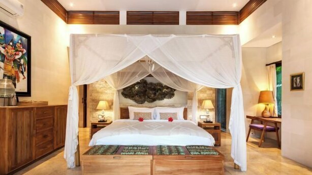 A spacious bedroom with a canopy bed, wooden nightstands, and a stone accent wall. - Villa Liang Ubud (Bali)