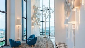 A modern hotel lobby with large windows, a white tree sculpture, and blue chairs. - Arte Cheras by KL Innfinity Stay (Kuala Lumpur)