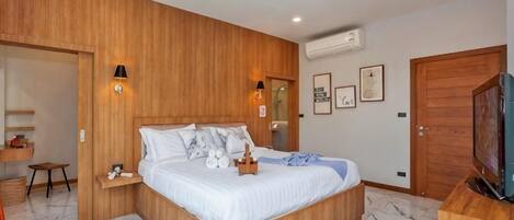 A bedroom with a wooden headboard, a bed with white bedding, a small bedside table, a television, and a wooden wardrobe.
