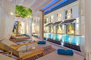 A poolside area with lounge chairs, a wooden table, and a view of a building with a swimming pool. - 9 bedroom Stylish 2-Villa Combination by Hi At Home (Pattaya)