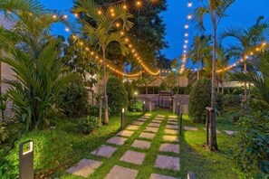A garden pathway with stepping stones, palm trees, and string lights. - 9 bedroom Stylish 2-Villa Combination by Hi At Home (Pattaya)