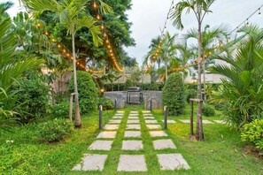 A garden pathway with stepping stones leading to a seating area, surrounded by lush greenery and palm trees. - 9 bedroom Stylish 2-Villa Combination by Hi At Home (Pattaya)