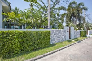 A modern building with a white exterior, a stone wall, and a well-maintained hedge. - 9 bedroom Stylish 2-Villa Combination by Hi At Home (Pattaya)