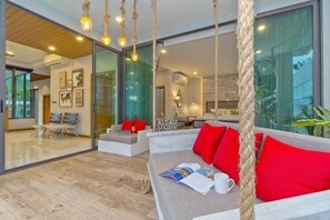 A modern living room with a sofa, red cushions, a magazine, and a hanging rope swing.