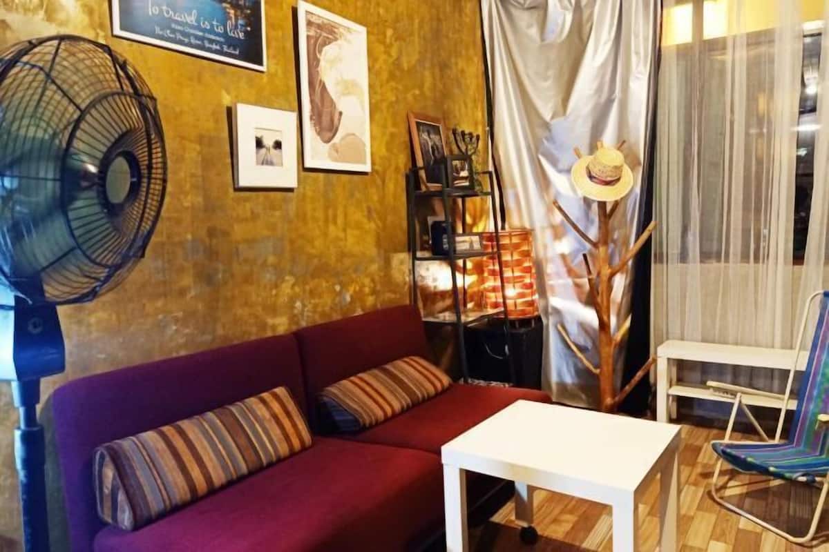 A cozy living room with a red sofa, a white table, a fan, and a bookshelf.