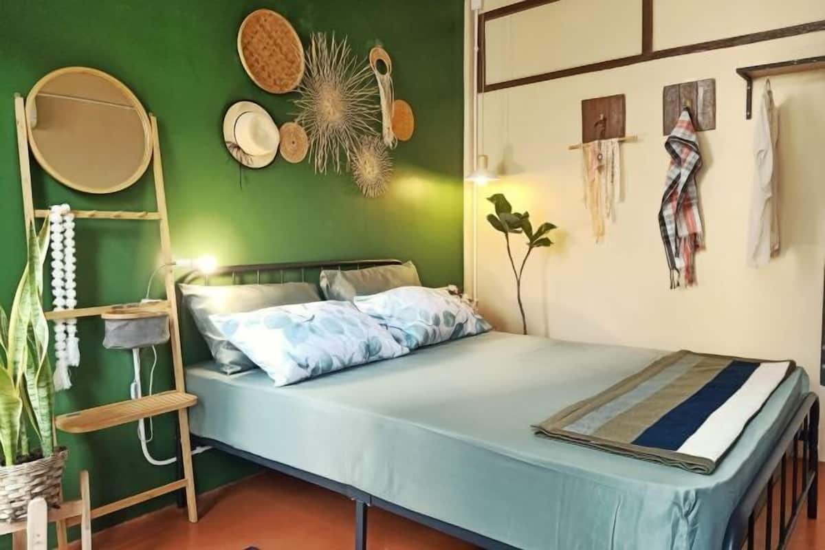 A bedroom with a bed, a bedside table, a mirror, and wall decorations including hats and a plant.