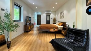 A modern bedroom with a bed, a black leather sofa, a wooden floor, and a potted plant. - OH Trendy homes Hoan Kiem LTK Bancony City view (Hanoi)
