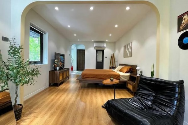 Une chambre à coucher moderne avec un lit, un canapé en cuir noir, un plancher en bois et une plante en pot.