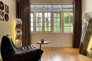 A room with a leather chair, a small round table, a window with curtains, and a wall-mounted art piece. - OH Trendy homes Hoan Kiem LTK Bancony City view (Hanoi)