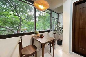 A room with a wooden table and chairs, a hanging light fixture, and a view of trees through large windows. - OH Trendy homes Ly Thuong Kiet (Hanoi)