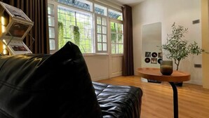 A room with a black leather sofa, a round wooden table with a vase, and a large window with curtains. - OH Trendy homes Hoan Kiem LTK Bancony City view (Hanoi)