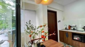 A modern kitchen with a wooden table, a vase with branches, and a view of the outside. - OH Trendy homes Hoan Kiem LTK Bancony City view (Hanoi)