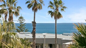 A hotel with a view of the ocean, palm trees, and a building with a flat roof.