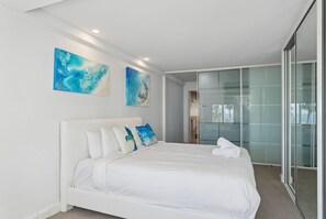 A modern bedroom with a white bed, a glass door closet, and abstract art on the wall.