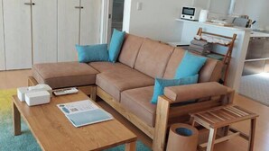 A modern living room with a brown sectional sofa, a wooden coffee table, and a small wooden side table. - Lapita Resort (Sakai)