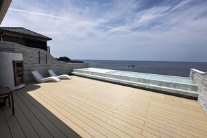 Terraza de madera con piscina y sillones de descanso, con vista al mar.